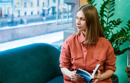 Woman holding book and sitting on couch looks hopefully out window