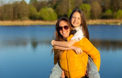 Woman giving daughter piggy back ride on lake shore